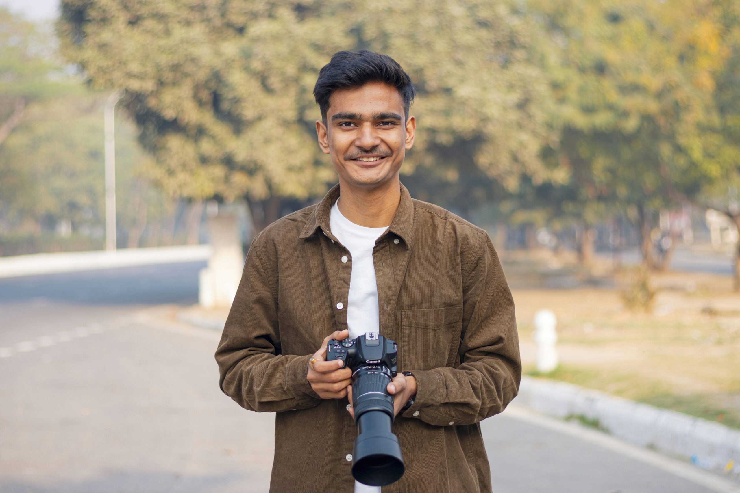 Smiling young photographer holding camera in sunny urban park setting.